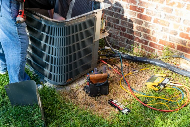 A close up view of an outdoor air conditioning unit being worked on by an HVAC technician.