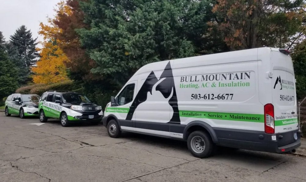 A white service van with a mountain logo parked beside smaller vehicles, set against colorful autumn trees.