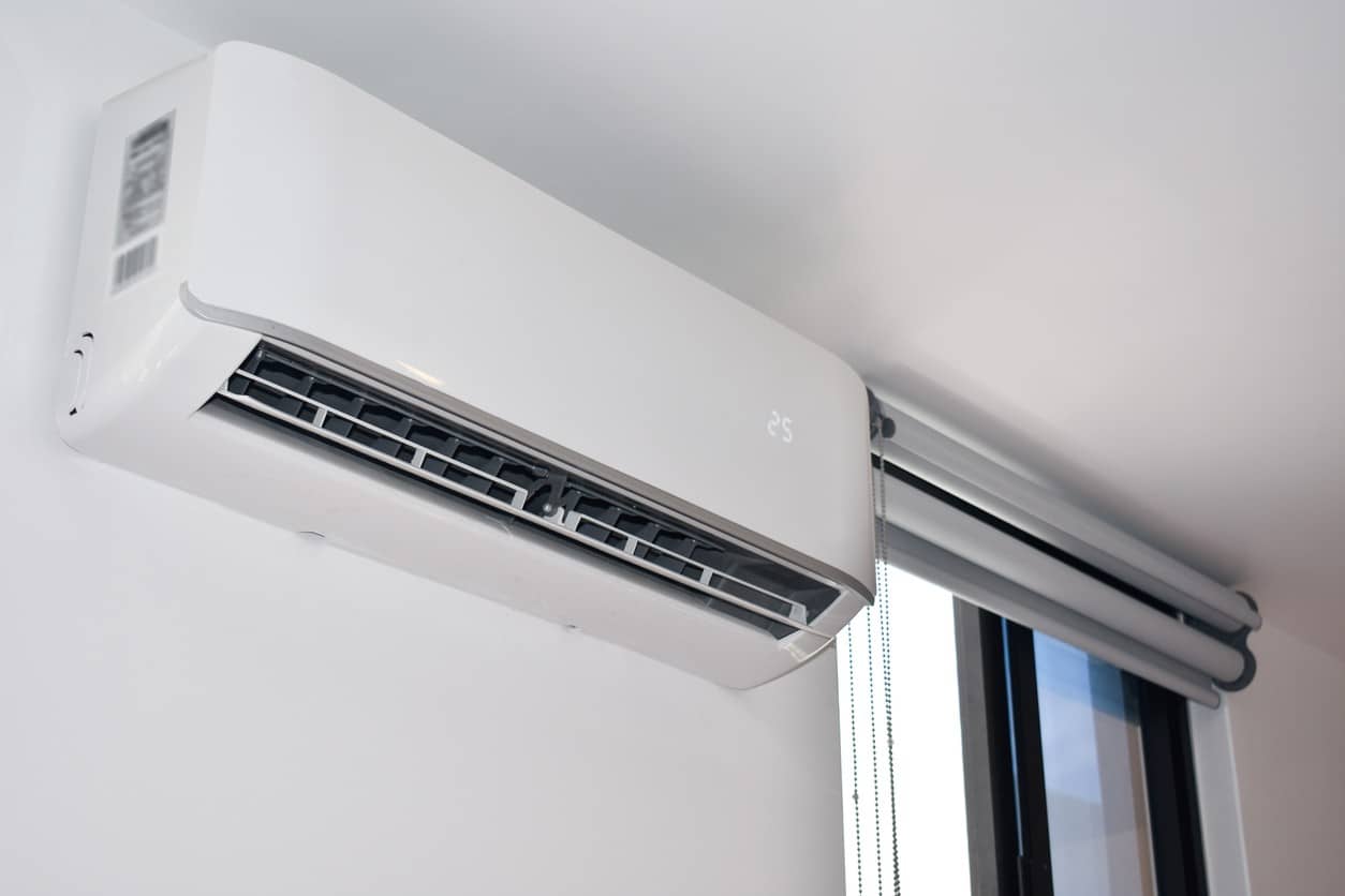 A modern air conditioning unit mounted on a wall near a window, featuring a sleek, minimalist design.