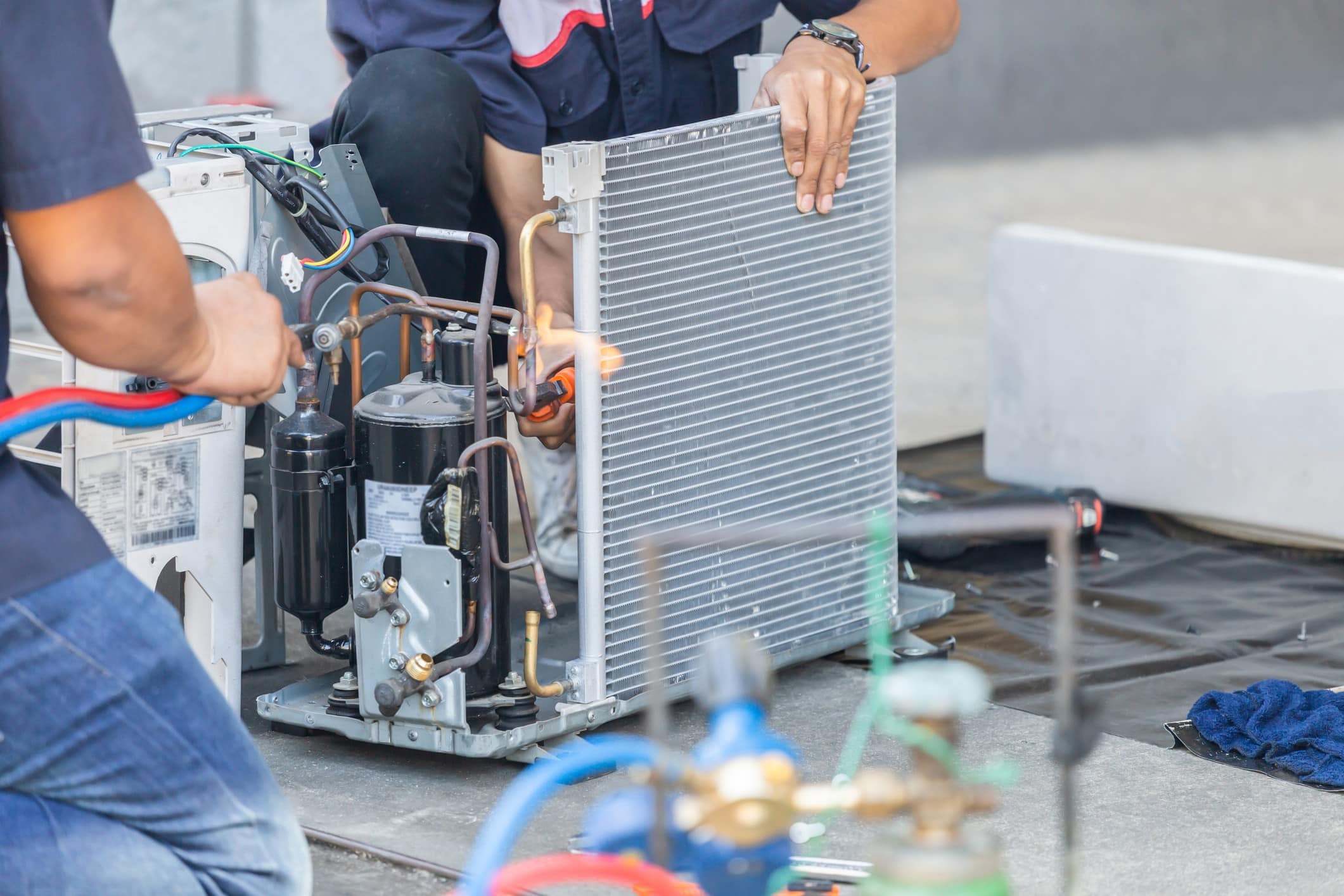 Technicians working on an air conditioning unit, handling components and using tools for maintenance or installation.